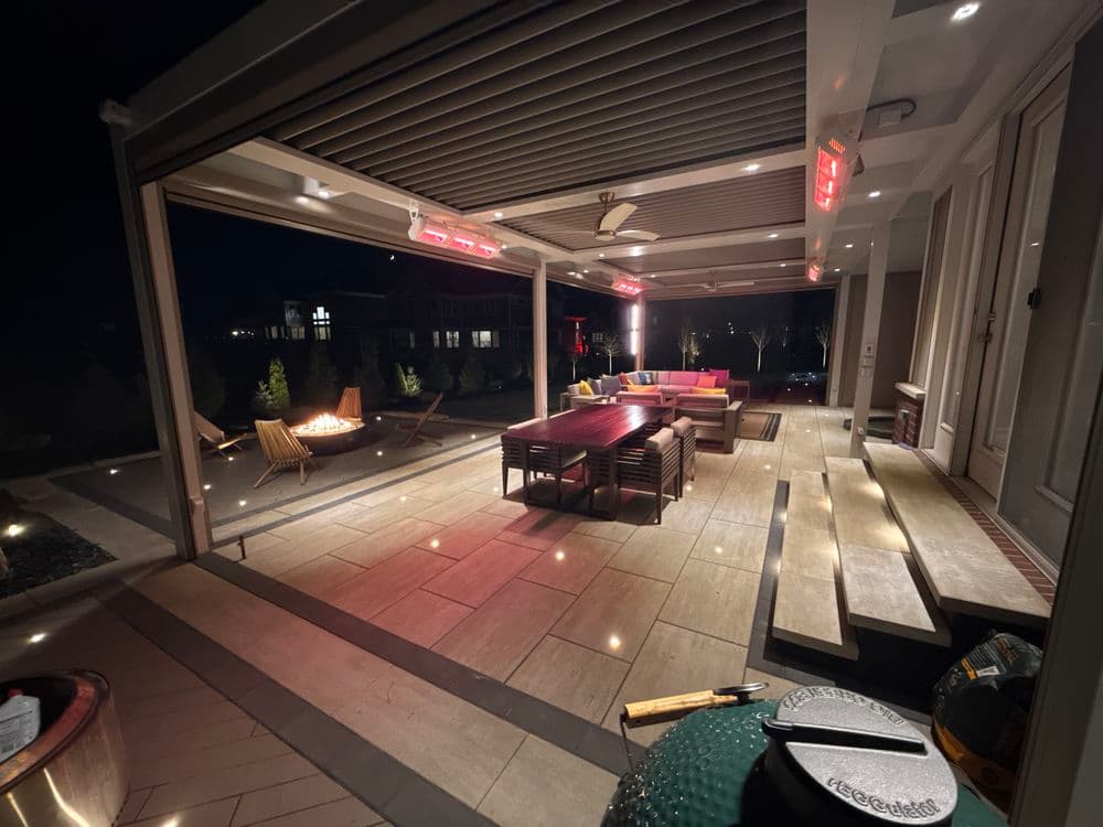 Modern outdoor patio with seating, a fire pit, and ambient lighting at night.