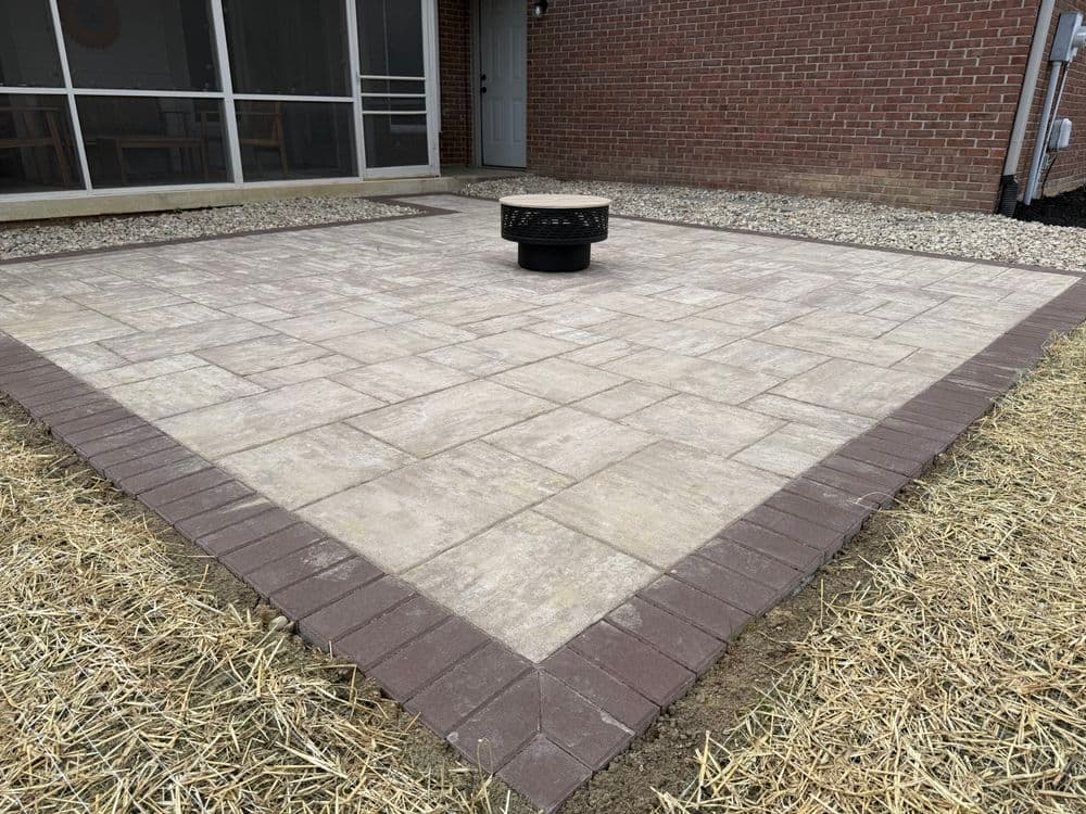 Paver patio with fire pit in a residential backyard, surrounded by straw.